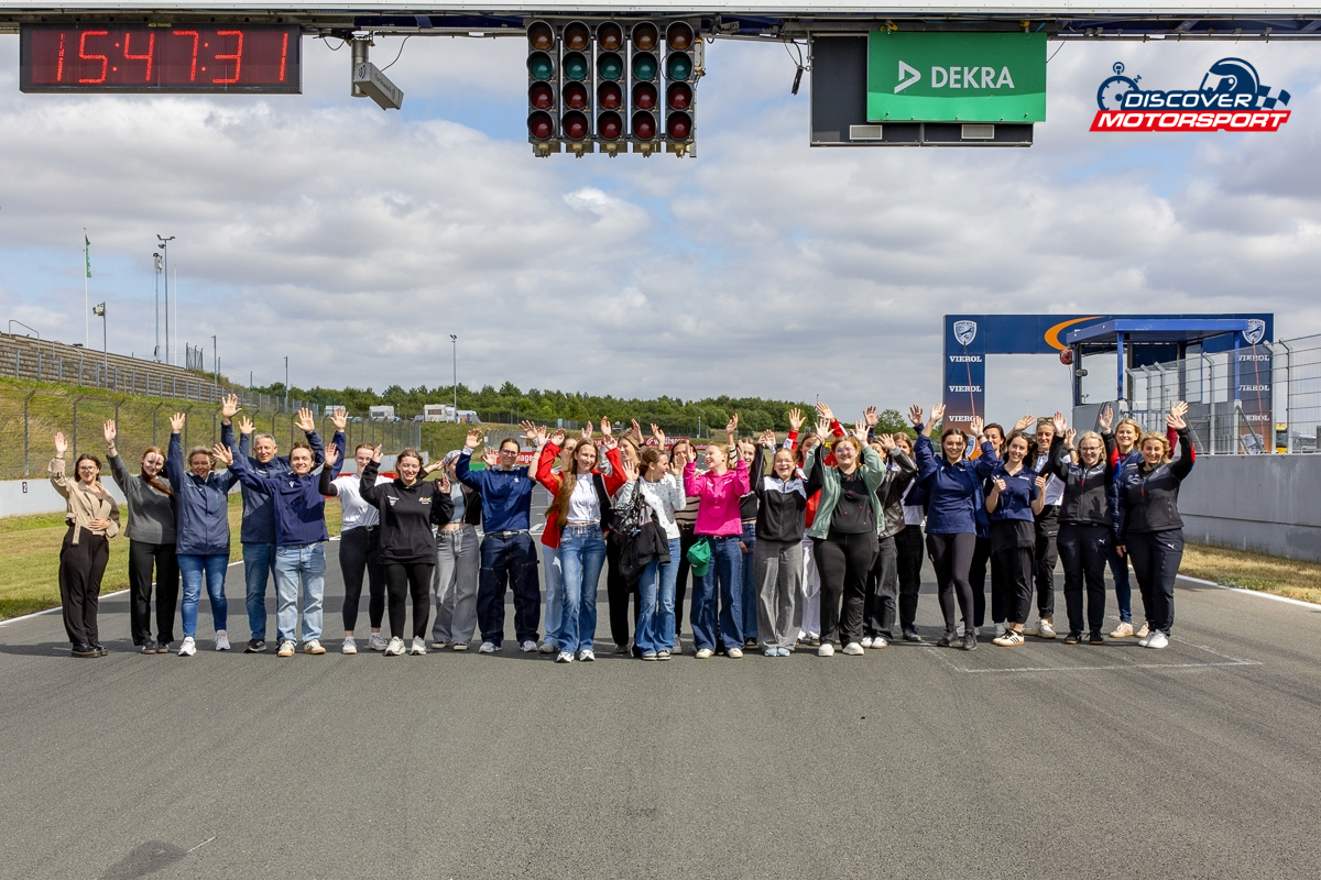 Teilnehmerinnen und Rednerinnen posieren gemeinsam für ein Gruppenfoto auf der Rennstrecke mit erhobenen Händen.